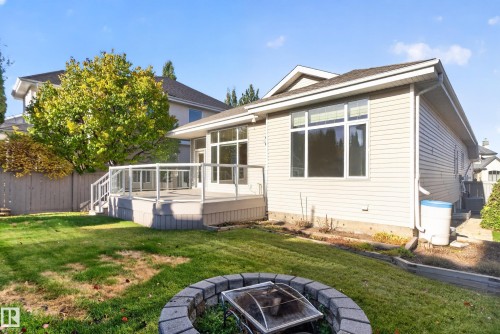 Rear exterior featuring light-toned horizontal siding, a raised deck with white glass-panel railings, large multi-pane windows, and a stone-block fire pit - 876 Twin Brooks Close Nw, Edmonton, AB 
