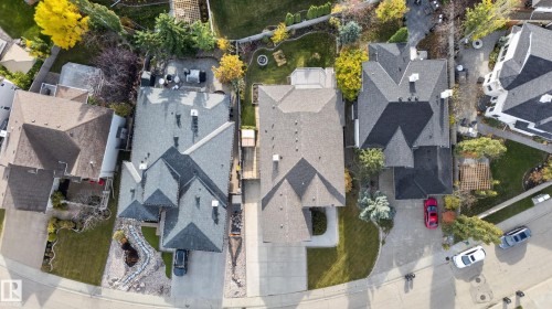 Aerial perspective of a multi-level residence featuring a multi-pitched roof, paved driveway, landscaped front yard with stone-border accents, and a fenced backyard with mature trees - 876 Twin Brooks Close Nw, Edmonton, AB 