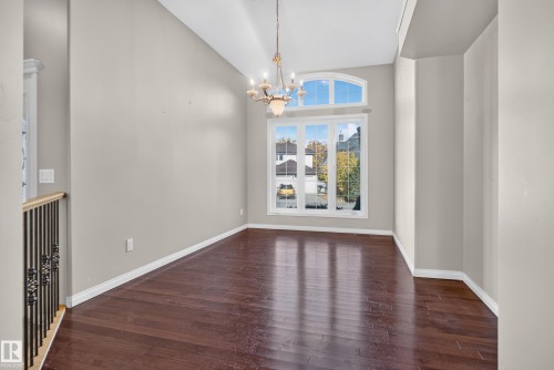 High-ceiling space featuring wood-finish flooring, a multi-light candelabra chandelier, and an expansive window assembly with an arched transom - 876 Twin Brooks Close Nw, Edmonton, AB 