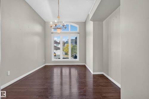 High-ceiling interior featuring wood-finish flooring, a multi-pane window with a prominent arched transom, and a tiered hanging chandelier - 876 Twin Brooks Close Nw, Edmonton, AB 