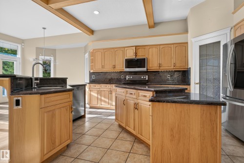Kitchen featuring light wood cabinetry, dark stone countertops, tile flooring, built-in stainless steel appliances, and decorative ceiling beams - 876 Twin Brooks Close Nw, Edmonton, AB 