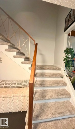 Staircase featuring light-toned carpeting and a wooden handrail with decorative metal balusters - 5 Gilmore Crescent, St. Albert, AB 