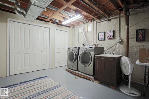 Dedicated laundry area featuring a utility sink and cabinetry, two bi-fold doors, and exposed ceiling joists - 5 Gilmore Crescent, St. Albert, AB 
