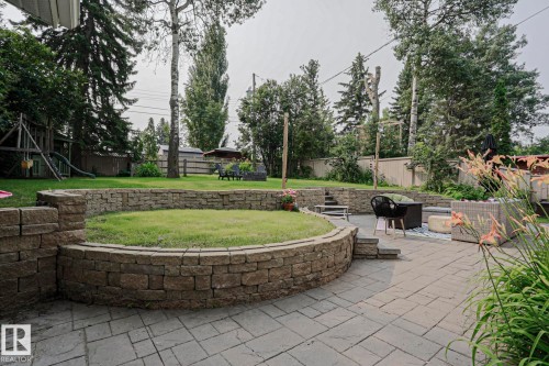 Expansive backyard featuring a stone paver patio, multi-level stone retaining walls, and mature perimeter trees - 5 Gilmore Crescent, St. Albert, AB 
