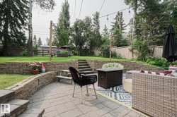 Multi-level backyard featuring a paver patio, stone retaining walls, and a manicured lawn - 