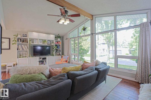Vaulted ceiling with exposed wood beam, large picture windows, wood-finish flooring, built-in entertainment center, and ceiling fan with light fixture - 5 Gilmore Crescent, St. Albert, AB 