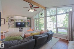 Vaulted ceiling with exposed wood beam, large picture windows, wood-finish flooring, built-in entertainment center, and ceiling fan with light fixture - 