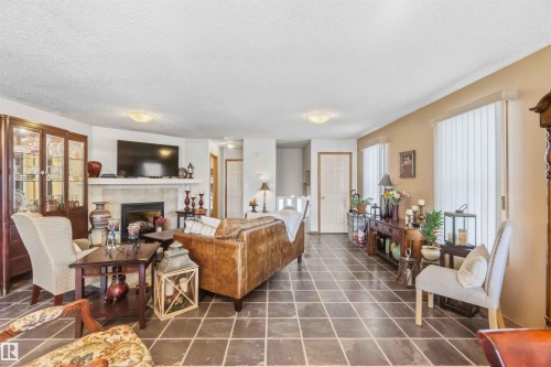 Living area featuring tile flooring, a fireplace with a neutral surround, vertical blinds, and two flush-mount ceiling light fixtures - 497 Kananaskis Drive, Devon, AB 