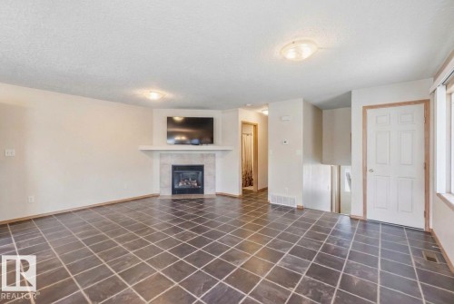 Interior area featuring large-format tile flooring, a corner fireplace with stone-surround hearth, a built-in mantle, and neutral wall tones - 497 Kananaskis Drive, Devon, AB 