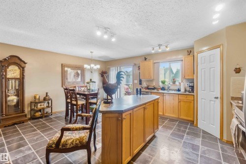 Kitchen featuring natural wood cabinetry, a center island with a solid-surface countertop, ceramic tile flooring, and multi-directional track lighting - 497 Kananaskis Drive, Devon, AB 