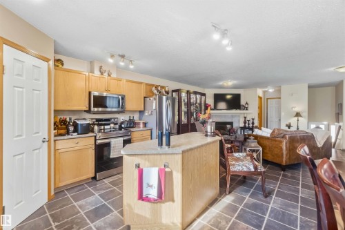 Kitchen featuring light-finish cabinetry, a center island with a solid surface countertop, stainless steel appliances, and slate-finish tile flooring - 497 Kananaskis Drive, Devon, AB 