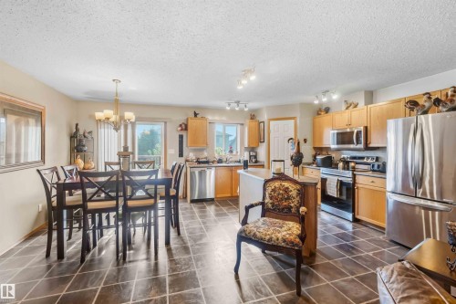 Open-concept kitchen and dining area featuring tile flooring, wooden cabinetry, stainless steel appliances, and a multi-light chandelier - 497 Kananaskis Drive, Devon, AB 