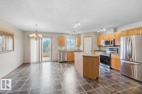 Kitchen featuring wood cabinetry, stainless steel appliances, a central island, tile flooring, and a glass sliding door - 497 Kananaskis Drive, Devon, AB 