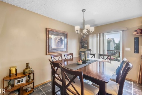 Dining area featuring tile flooring, a multi-arm chandelier with frosted glass shades, and a sliding glass door providing external access - 497 Kananaskis Drive, Devon, AB 