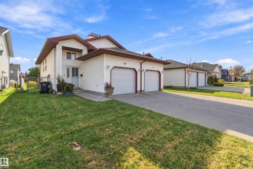Two-story residence featuring light-toned vinyl siding, dual attached garages, a paved driveway, and a front-facing chimney - 497 Kananaskis Drive, Devon, AB 
