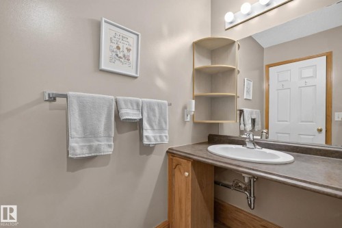Vanity featuring a solid surface countertop, inset oval basin with a metal faucet, built-in corner shelving, and a multi-bulb light fixture above a wall-mounted mirror - 497 Kananaskis Drive, Devon, AB 