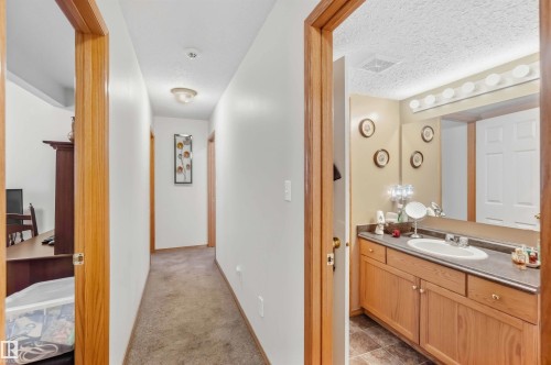 Bathroom featuring a wood-tone vanity, solid surface countertop with an integrated sink, full-width vanity mirror, and linear vanity lighting - 497 Kananaskis Drive, Devon, AB 