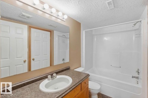 Virtually Decluttered- Full-width vanity mirror, integrated sink countertop, wood cabinetry, and a white acrylic tub-shower combination - 497 Kananaskis Drive, Devon, AB 