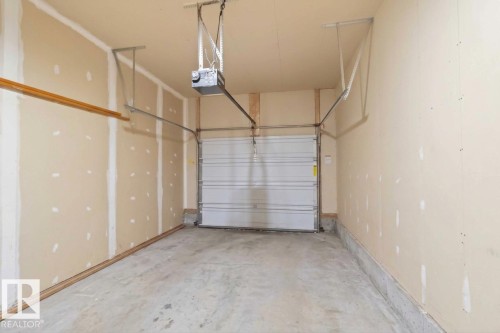 Enclosed garage space featuring painted drywall, concrete flooring, and an automated overhead door opener - 497 Kananaskis Drive, Devon, AB 