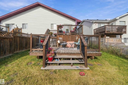 Multi-level wood deck featuring black metal railings, lattice privacy screening, and stairs leading to a backyard lawn - 497 Kananaskis Drive, Devon, AB 