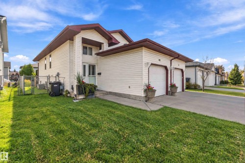 Bi-level exterior featuring light horizontal siding, dual-car garage, concrete driveway, and side chain-link fencing - 497 Kananaskis Drive, Devon, AB 