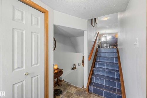 Entryway featuring a bifold closet, tile flooring, and a staircase with tiled treads and a wood handrail - 497 Kananaskis Drive, Devon, AB 