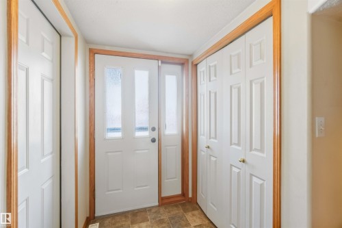 Entryway featuring a front door with two vertical textured glass panels, a matching glass sidelight, bi-fold closet doors, and wood-finish door trim - 497 Kananaskis Drive, Devon, AB 