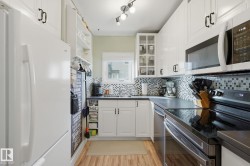White cabinetry with black hardware, mosaic tile backsplash, wood-finish flooring, recessed lighting, and built-in microwave - 