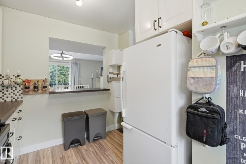 White cabinetry with dark hardware, pass-through window, wood-finish flooring, and light wall paint - 5340 38A Avenue Nw, Edmonton, AB 