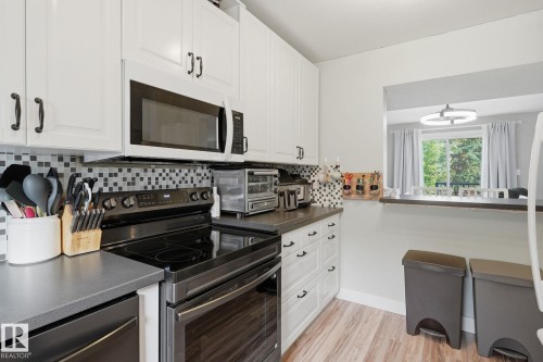 White shaker-style cabinetry with dark hardware, black electric range, over-the-range microwave, gray countertops, and wood-finish flooring - 5340 38A Avenue Nw, Edmonton, AB 