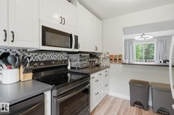 White shaker-style cabinetry with dark hardware, black electric range, over-the-range microwave, gray countertops, and wood-finish flooring - 