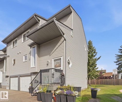 Multi-level exterior with horizontal siding, two integrated garage doors, an elevated entrance with black metal railings, and a prominent front bay window - 5340 38A Avenue Nw, Edmonton, AB 