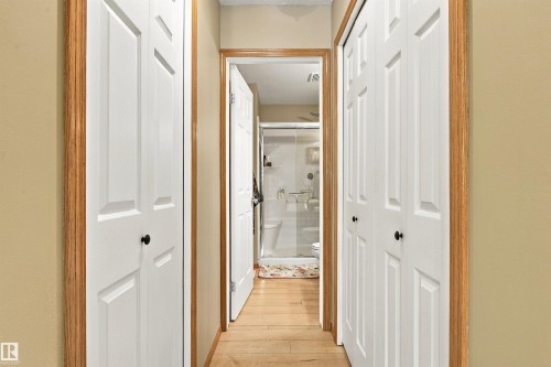 Hallway with wood-finish flooring, light-colored walls, and white bi-fold closet doors with black hardware - 51064 Rge Rd 222, Rural Strathcona County, AB 