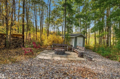 Paved patio with a built-in fire pit, surrounded by a gravel ground cover and mature trees, featuring a wood-sided storage shed - 51064 Rge Rd 222, Rural Strathcona County, AB 