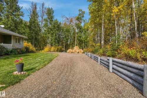 Gravel driveway featuring a log retaining wall, surrounded by mature trees and a manicured lawn - 51064 Rge Rd 222, Rural Strathcona County, AB 