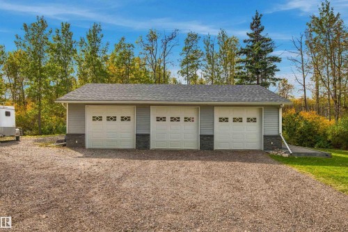 Detached triple garage with white panel doors featuring decorative window inserts, light gray siding, dark stone veneer skirting, and a shingle roof - 51064 Rge Rd 222, Rural Strathcona County, AB 