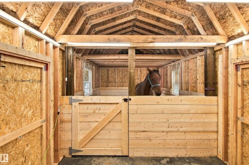Wood-framed stable structure featuring multiple stalls, exposed wood beams, and integrated lighting fixtures - 51064 Rge Rd 222, Rural Strathcona County, AB 