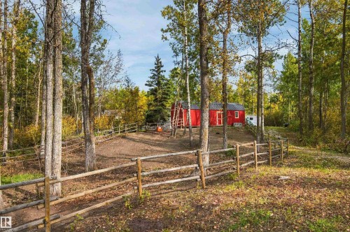 Red-sided structure with a gray roof and white trim windows, surrounded by mature trees and natural landscaping, featuring a wooden split-rail fence - 51064 Rge Rd 222, Rural Strathcona County, AB 