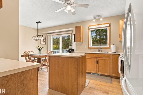 Kitchen and dining area featuring wood-finish cabinetry, light-toned countertops, a center island, wood-finish flooring, and a sliding glass door - 51064 Rge Rd 222, Rural Strathcona County, AB 
