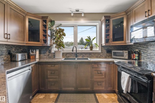 Kitchen featuring wood cabinetry with integrated wine storage, mosaic tile backsplash, and dual-basin sink with matte black fixture - 6207 85 Avenue Nw, Edmonton, AB 