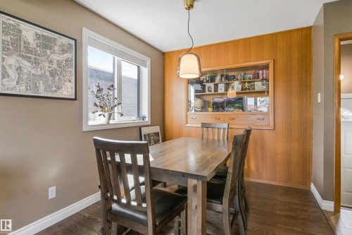 Wood-finish flooring, wood-paneled accent wall, built-in display cabinetry with glass shelving, and a pendant light fixture - 6207 85 Avenue Nw, Edmonton, AB 