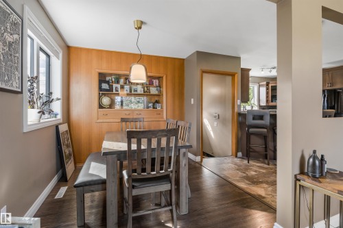 Dining space featuring wood-paneled walls, built-in display cabinetry, wood-finish flooring, and a pendant light fixture - 6207 85 Avenue Nw, Edmonton, AB 