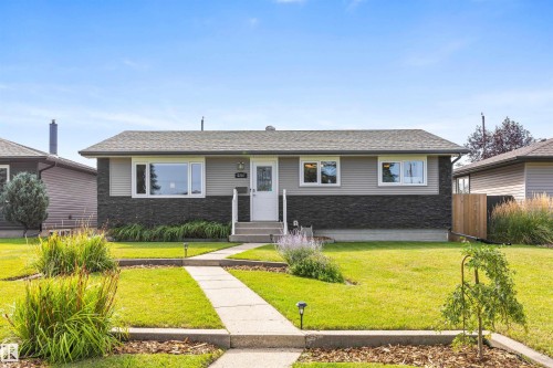 Single-story exterior featuring a grey lap-siding upper facade with dark-toned stone veneer lower cladding, and concrete walkway. - 6207 85 Avenue Nw, Edmonton, AB 