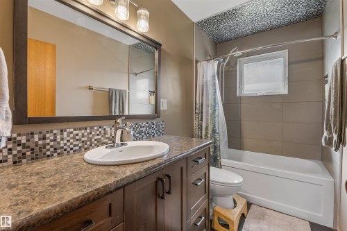 Bathroom featuring dark wood-finish cabinetry, an oval sink, a stone-pattern laminate countertop, a mosaic tile backsplash, and a tiled shower surround with a decorative tile ceiling accent - 6207 85 Avenue Nw, Edmonton, AB 
