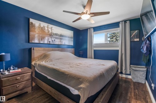 Bedroom featuring dark-toned walls, wood-finish flooring, and a ceiling-mounted fan with integrated lighting - 6207 85 Avenue Nw, Edmonton, AB 