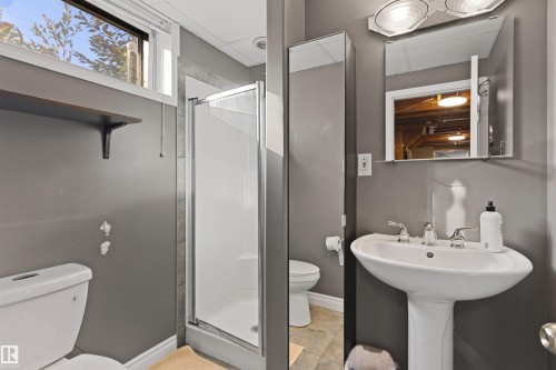 Bathroom featuring a white pedestal sink with metal fixtures, a walk-in shower with a glass door, a wall-mounted medicine cabinet, and a vertical storage column - 6207 85 Avenue Nw, Edmonton, AB 