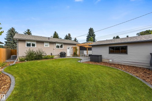 Backyard featuring a manicured lawn, stone-paver patio, wooden pergola, and wood-paneled fencing - 6207 85 Avenue Nw, Edmonton, AB 