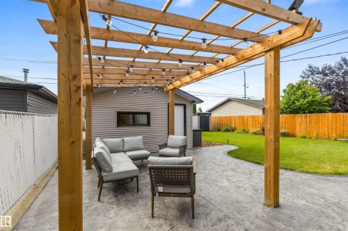 Custom wood-frame pergola with overhead string lighting, stamped concrete patio, manicured lawn, and wood privacy fencing - 6207 85 Avenue Nw, Edmonton, AB 