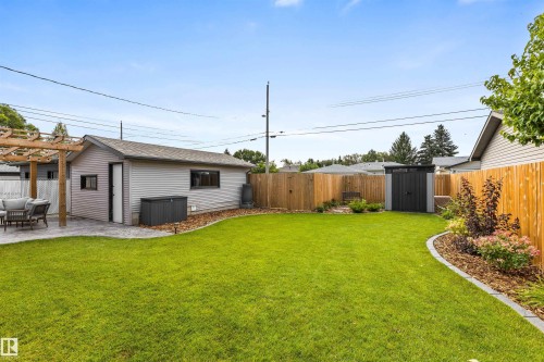 Backyard featuring a manicured lawn, wood-slat privacy fencing, detached garage, timber-frame pergola, and landscaped garden beds with stone edging - 6207 85 Avenue Nw, Edmonton, AB 
