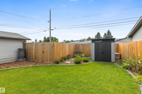 Fenced backyard featuring a manicured lawn, wood-tone privacy fencing, mature landscaping, and a detached storage structure - 6207 85 Avenue Nw, Edmonton, AB 